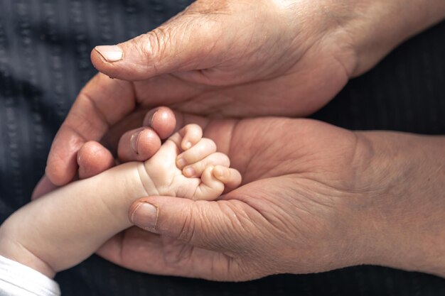 The handle of a newborn in the hands of a grandmother closeup