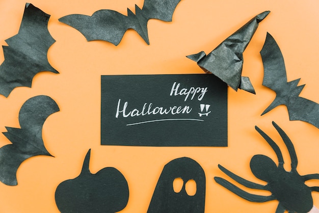 Foto gratuita pipistrelli e ragno fatti a mano con zucca scura e fantasma che giace intorno all'iscrizione felice alloween