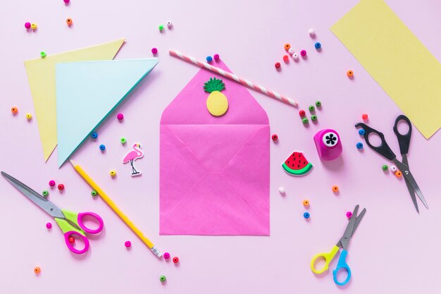 Handmade envelope surrounded with decorative items on pink background