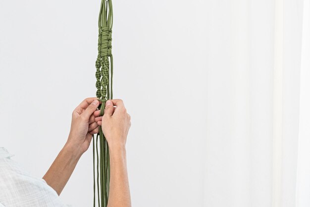На руке женщины вешают зеленые вешалки для растений макраме с горшечным растением. внутри макраме - горшок и растение монстера.