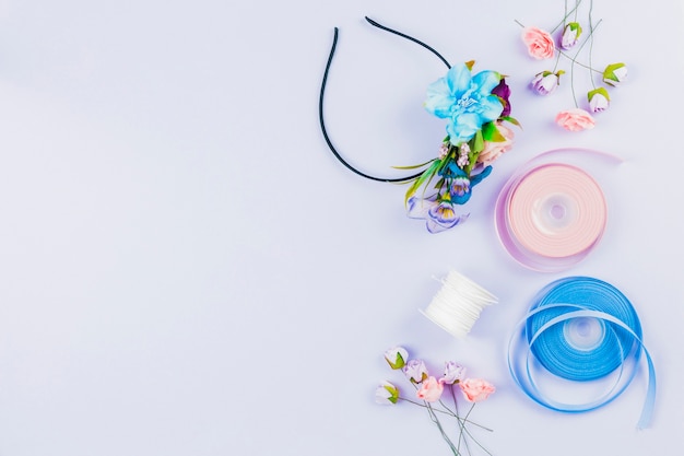 Handmade hairband made with artificial flowers; spool and ribbon on white backdrop