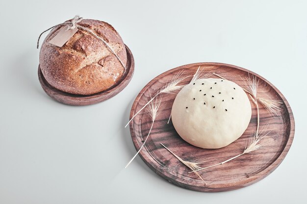 Handmade round bread bun dough with a cooked one in a wooden platter.