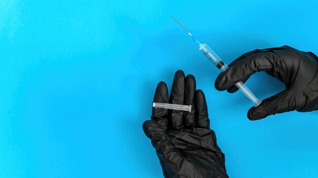 Hands in black medical gloves holding needle. Blue background. Top view