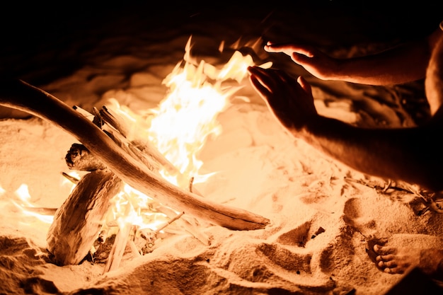 Foto gratuita mani vicino al fuoco sulla spiaggia