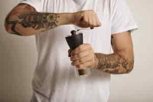 Free photo hands and chest of a tattooed young man grinding coffee in a manual burr grinder