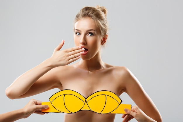 Foto gratuita mani che coprono ragazza bionda con costume da bagno giallo su sfondo bianco