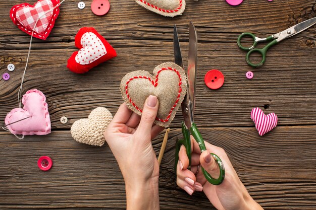 Hands cutting a red heart shape on wooden background