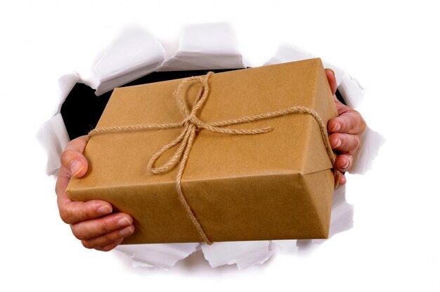 Hands delivering package through torn white paper background