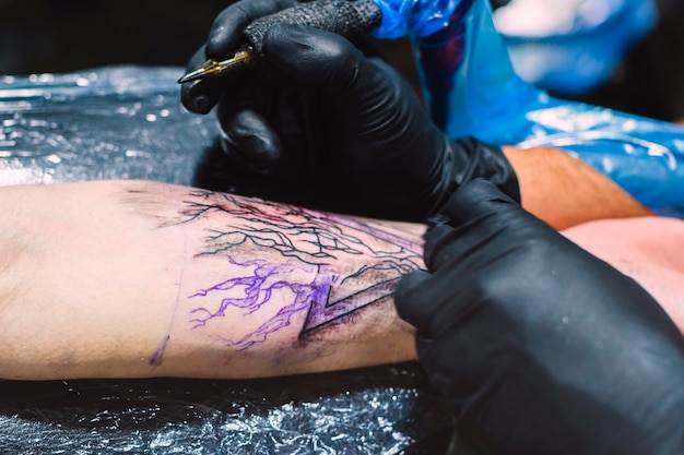 Hands drawing tattoo with machine on arm 