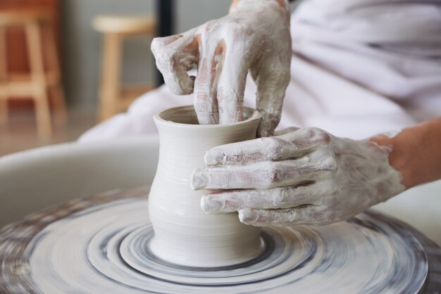 ワークショップで糸車に粘土の花瓶を作る女性陶工の手