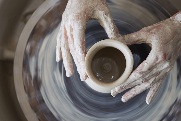 Free photo hands of female potter sculpting clay vessel on spinning wheel