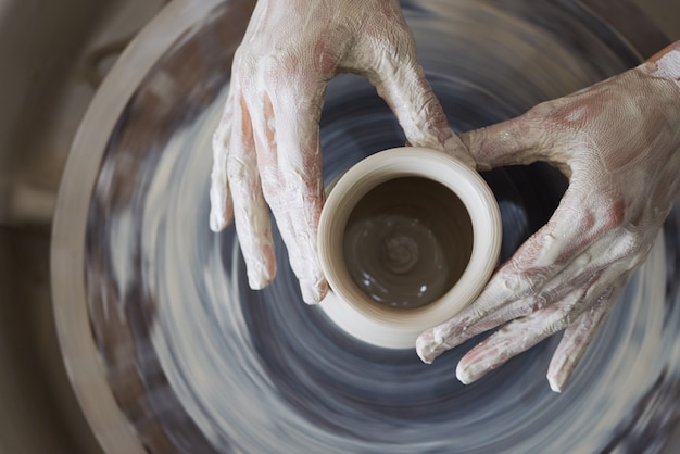 Руки женщины гончара лепят глиняный сосуд на прялке