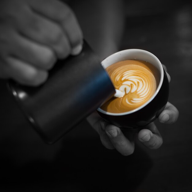 Hands filling a cup of coffee with milk