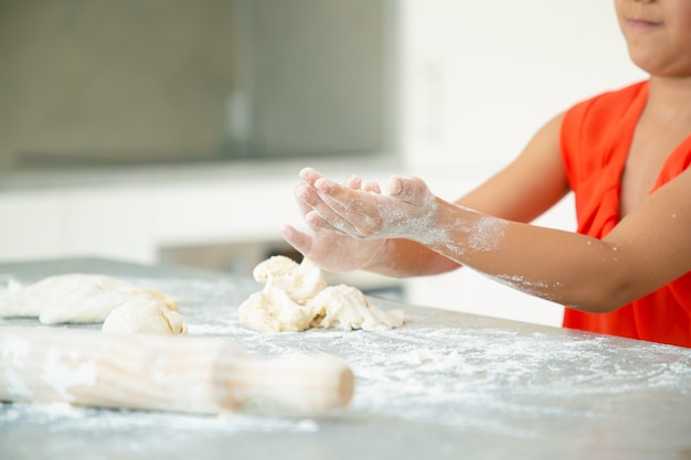 Руки девушки замешивают тесто на кухонном столе с грязной мукой. Малыш сам пекёт булочки или пироги. Средний план. Концепция семейной кухни