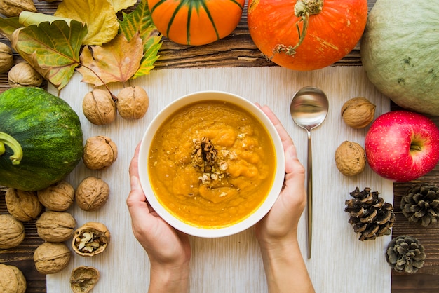 Hands holding bowl of pumpkin soup with walnuts