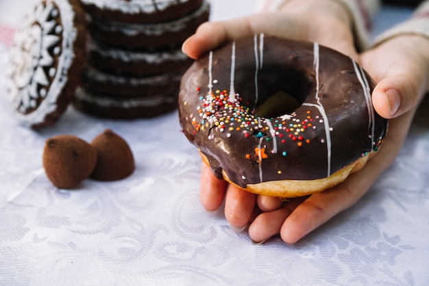 Hands holding chocolate donut with sprinkle on table cloth