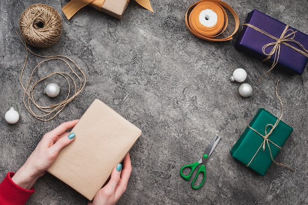 Hands holding christmas gift box with string and sacissors