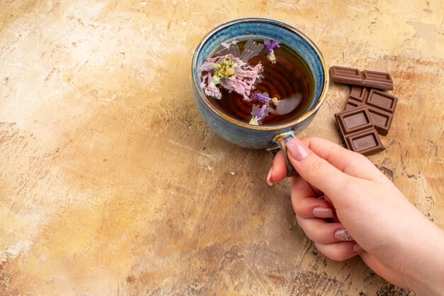 Руки держат чашку горячего травяного чая и плитки шоколада на столе смешанного цвета