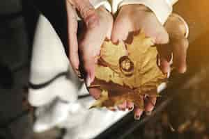 Free photo hands holding a dry leaf with two wedding rings