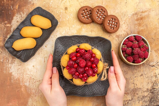 Hands holding freshly baked gift cake on a brown plate on mixed color table horizontal view