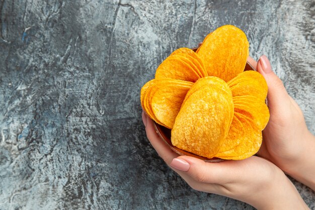 Hands holding homemade delicious crispy chips in a brown bowl on gray table