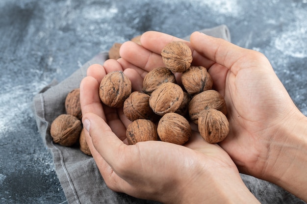 Free photo hands holding many of healthy walnuts on a marble surface.