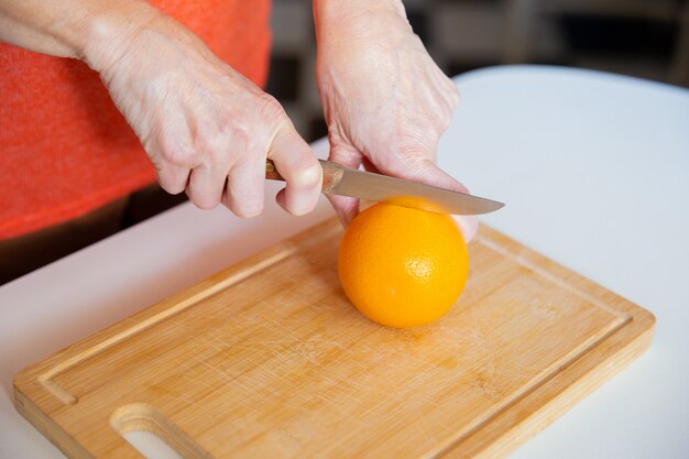 Руки держат апельсин и режут ножом