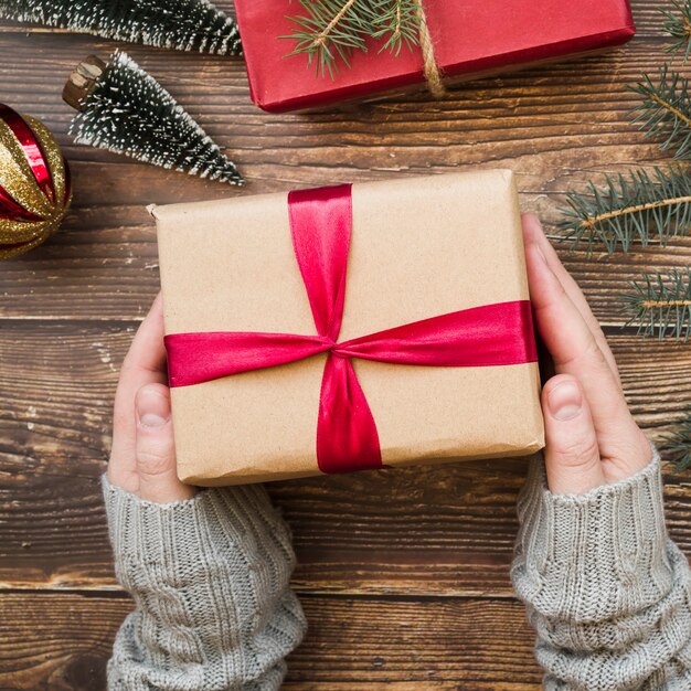 Hands holding present box near Christmas ball and fir twigs