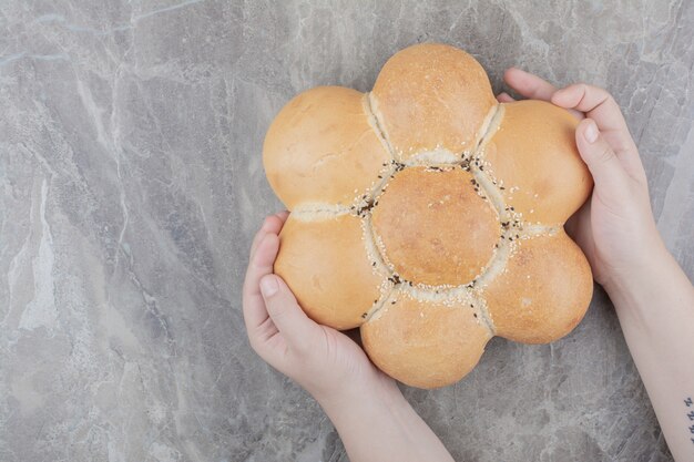 Foto gratuita mani che tengono un pane rotondo sulla superficie di marmo