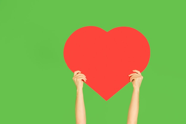 Hands holding the sign of heart on green  wall.