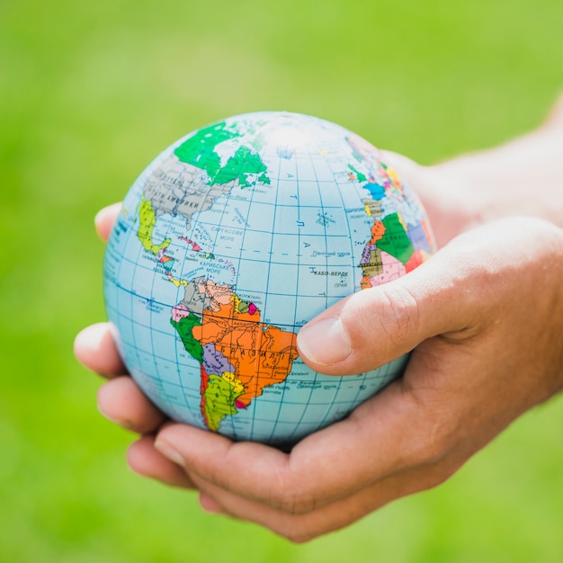 Hands holding small globe against green background