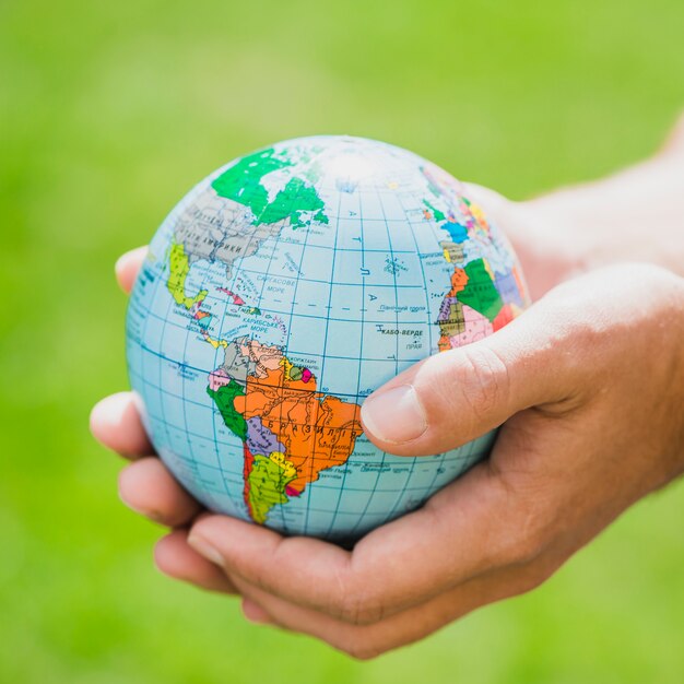 Hands holding small globe against green background