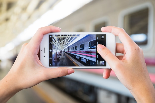 Hands holding smartphone on platform near train 