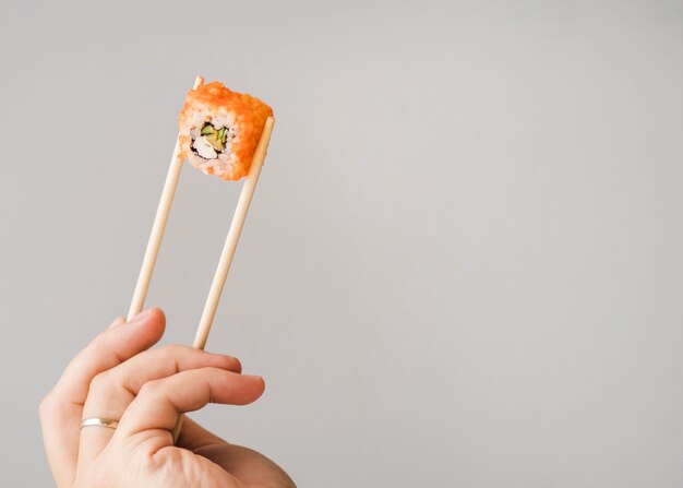 Hands holding sushi roll with chopsticks copy space