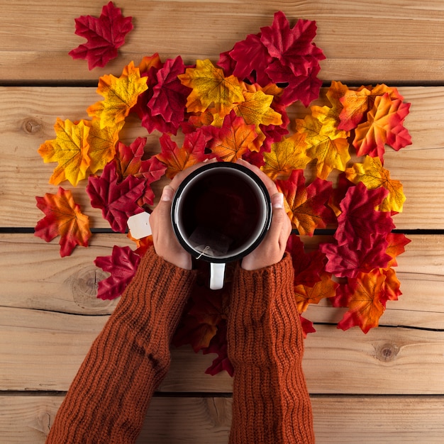 Free photo hands holding a tea with autumn leaves