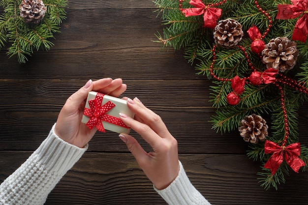 Hands holding a white gift box with pine tree around