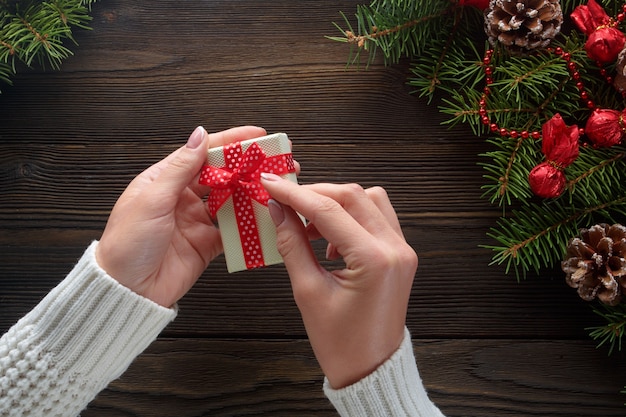 Hands holding a white gift box with pine tree around