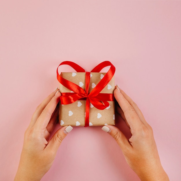 Hands holding wrapped gift with red ribbon