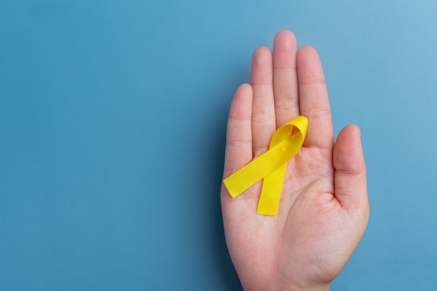 Hands holding yellow ribbon, symbol of cancer awareness, medical support and prevention with helping hand.