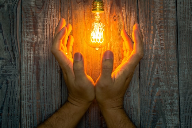 Hands next to a lit light bulb