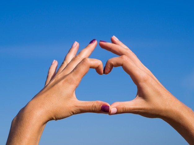 Free photo hands making a heart shape in the sky