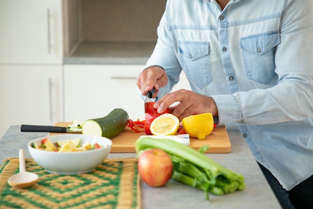 Foto gratuita mani dell'uomo che cucina insalata, tagliare le verdure fresche sul tagliere in cucina. colpo ritagliato, primo piano. concetto di cibo sano