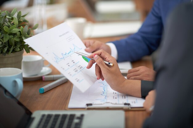 Hands of man and woman in business attire sitting at desk in office and discussing graph