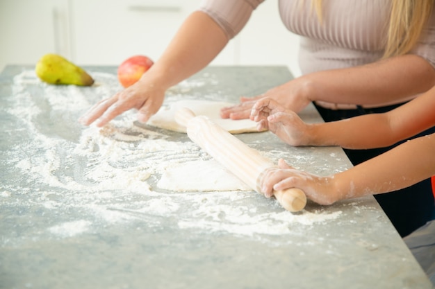 ママとキッチンのテーブルに生地を圧延の娘の手。少女と母親が一緒にパンやケーキを焼きます。クローズアップ、クロップドショット。家族の料理のコンセプト