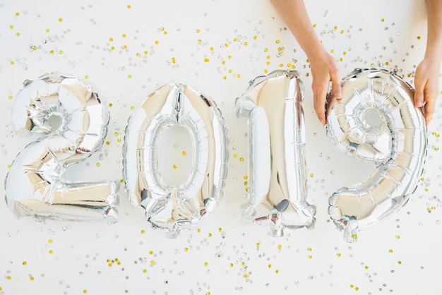 Hands near balloons numbers between confetti