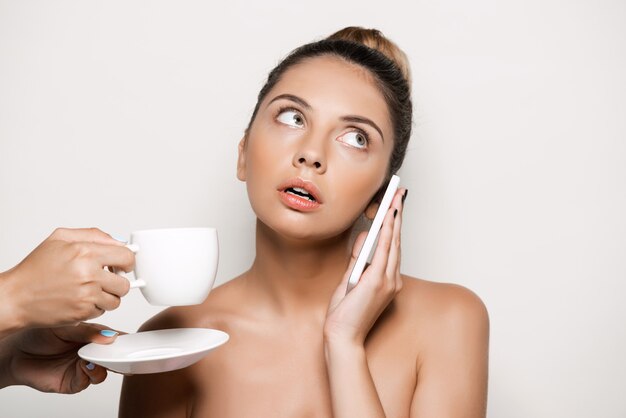 Hands offering cup of coffee to woman speaking on phone