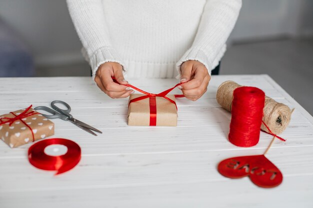 Hands packing gift with red ribbon on table