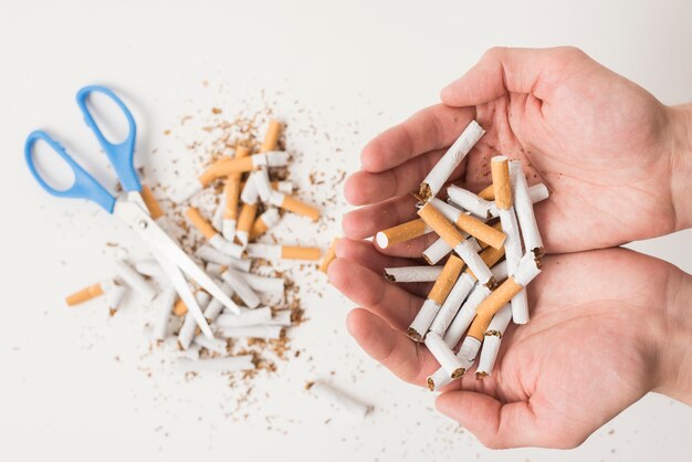 Hands of a person holding broken cigarettes over scissor and broken cigarettes