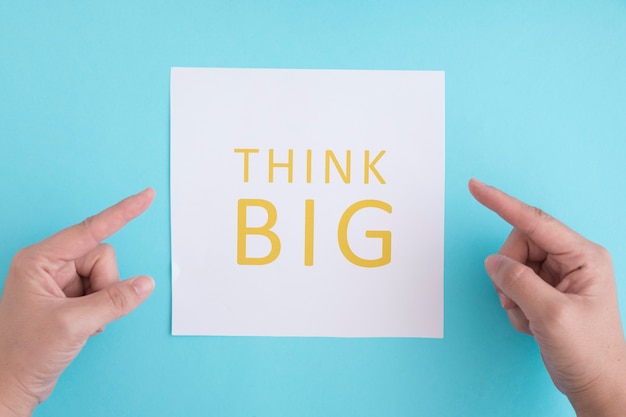 Hands pointing the finger on think big text over the white paper against blue background