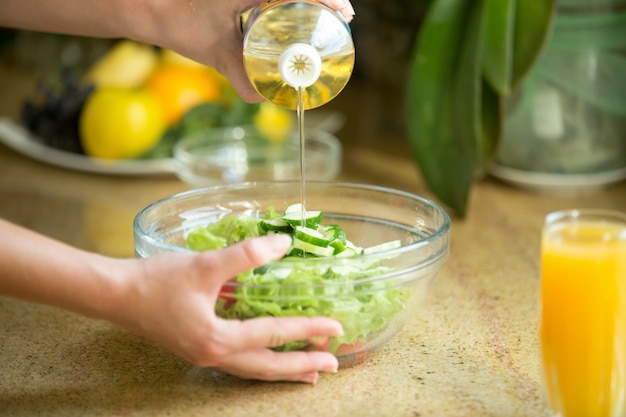 Руки, наливающие масло в зеленый салат